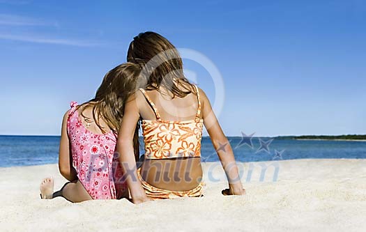 Two girls sitting on the sand looking at the sea