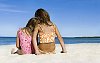 Two girls sitting on the sand looking at the sea