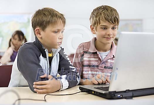 Two schoolboys with a laptop in the classroom