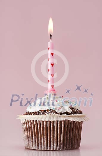 Cupcake with a lit candle on a pink background