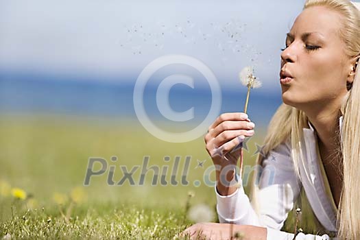 Woman on the grass blowing air to the dandelion