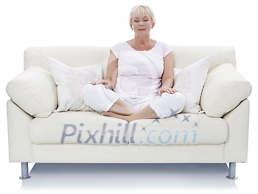 Isolated older woman sitting on the couch and meditating Isolated older woman sitting on the couch and meditating