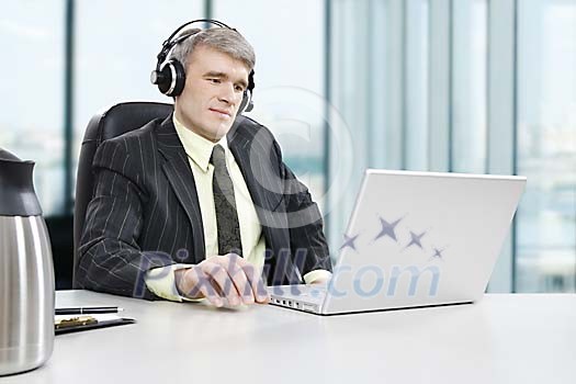 Businessman sitting behind his desk, listening to music