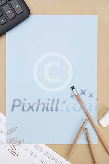 Empty blue paper surrounded by pencils, paper clips and calculator Empty blue paper surrounded by pencils, paper clips and calculator
