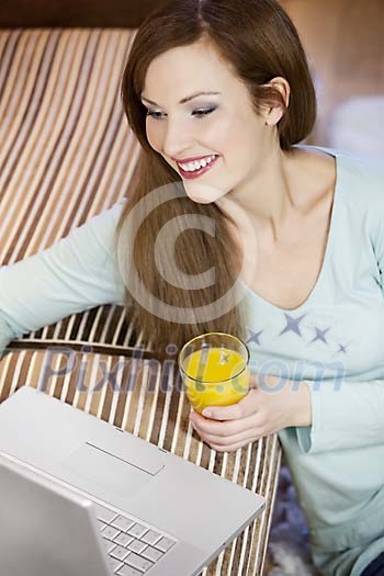 Woman sitting on the floor next to the couch with laptop and a glass of juice