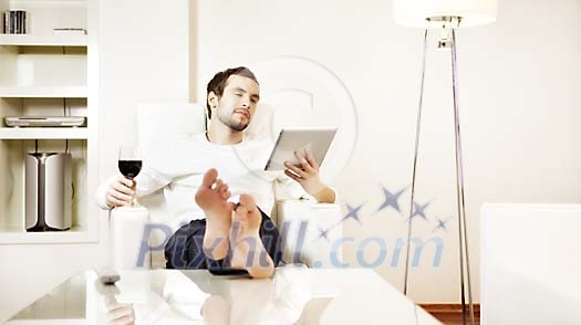 Man sitting in armchair with glass of wine reading tablet