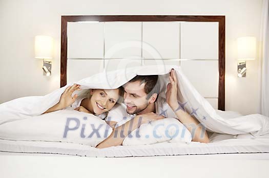 Couple hiding under the blanket on the bed
