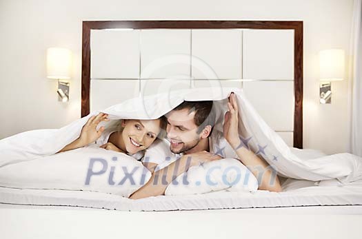 Couple hiding under the blanket on the bed Couple hiding under the blanket on the bed