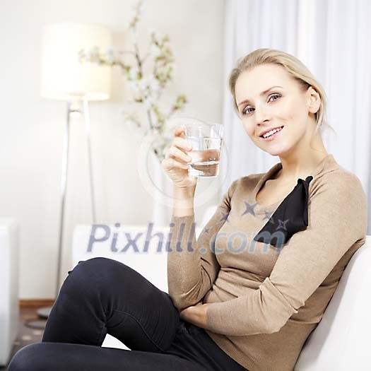 Woman holding a glass of water and sitting on the sofa