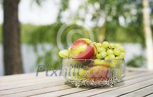 Apples and grapes in a bowl on a sunny table outside