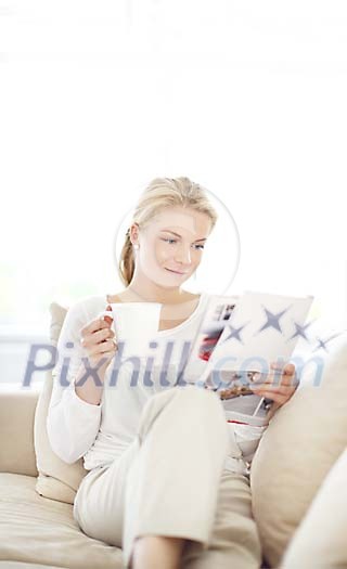 Woman sitting on the couch reading a magazine and drinking coffee