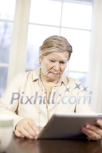 Senior woman reading at home from tablet computer