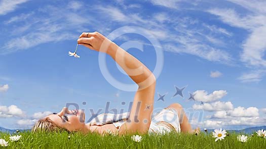 Woman lieing on the grass, looking at the daisy