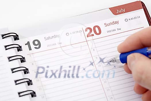 Hand writing a note on calendar for July 20