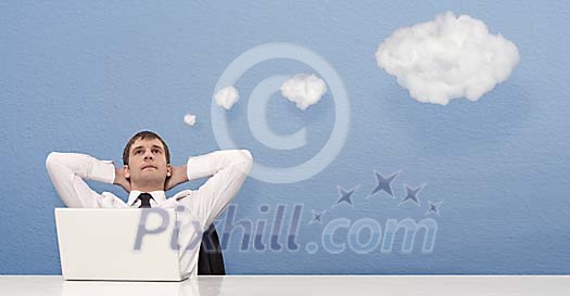 Businessman dreaming behind laptop under clouds in shape of thought bubbles