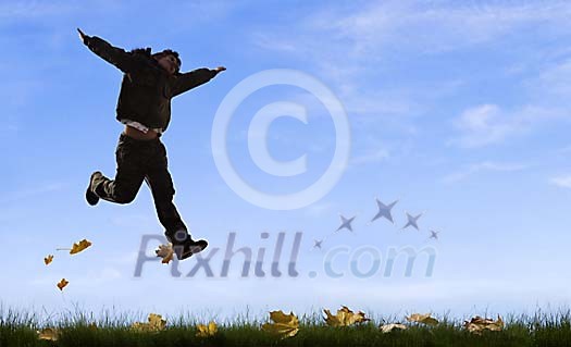 Boy jumping in grass with fallen maple leafs
