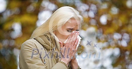 Blonde woman blows nose in autumn park Blonde woman blows nose in autumn park