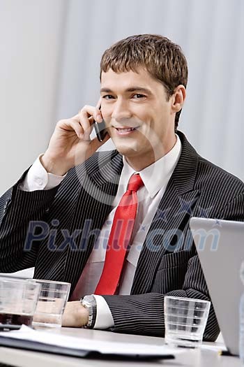 Business man speaking to mobile phone behind a meeting table