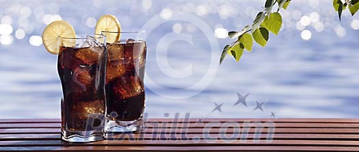 Glasses of soft drink on a table by a blue lake