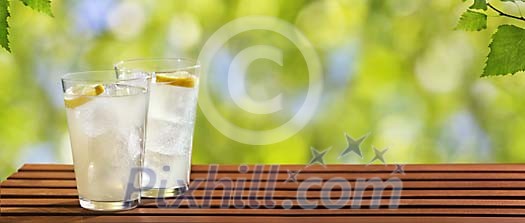 Glasses of lemonade on a table in green garden panorama