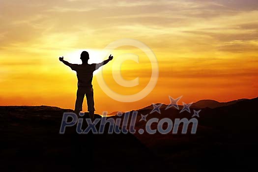 Man standing on a mountain hands spread towards sunset Man standing on a mountain hands spread towards sunset