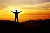 Man standing on a mountain hands spread towards sunset