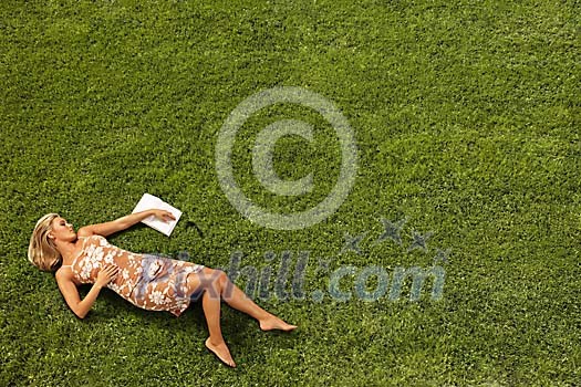 Young woman lying on lawn with a novel