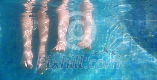 Two pair of feet under the water at the pool