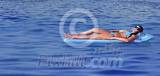 Woman sun tanning on a swimming matress on the sea