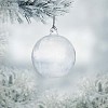 Transparent christmas ball hanging on a frozen fir outside seen through the window