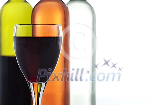 Wineglass filled with red wine in front of red, white and rose winebottles