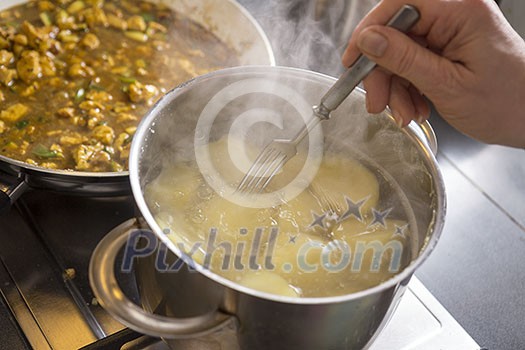 Potatos in a boiling water with hand checking with a fork of their readiness Potatos in a boiling water with hand checking with a fork of their readiness