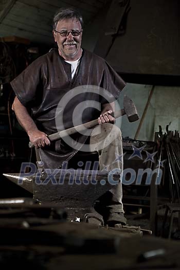 50-year old blacksmith holding a hammer by big anvil 50-year old blacksmith holding a hammer by big anvil