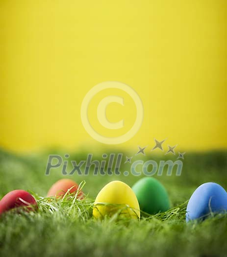Coloured easter eggs on grass, yellow background