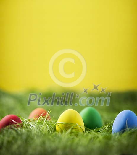 Coloured easter eggs on grass, yellow background Coloured easter eggs on grass, yellow background
