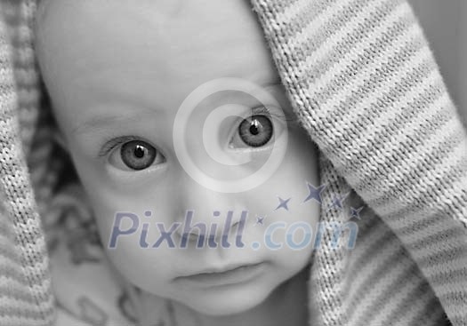 Big-eyed baby looking under the towel