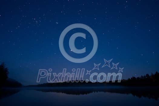 Stars shining over the lake and forest in the night