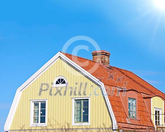 Yellow wooden house with red tiles and a blue sky with sunshine