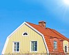 Yellow wooden house with red tiles and a blue sky with sunshine
