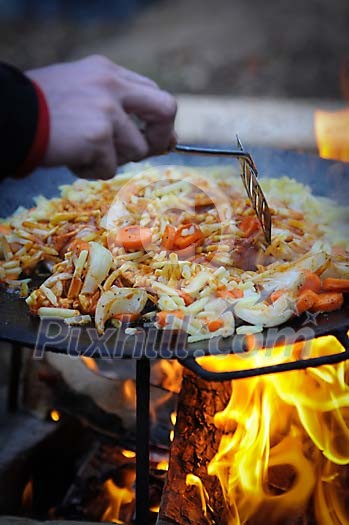 Hand mixing food on a campfire pan Hand mixing food on a campfire pan