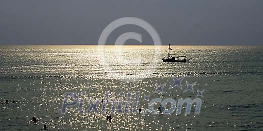 People swimming with a boat on the background at the sunset