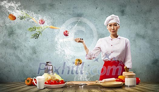 Asian female cook with knife cutting fruits and vegetables in air