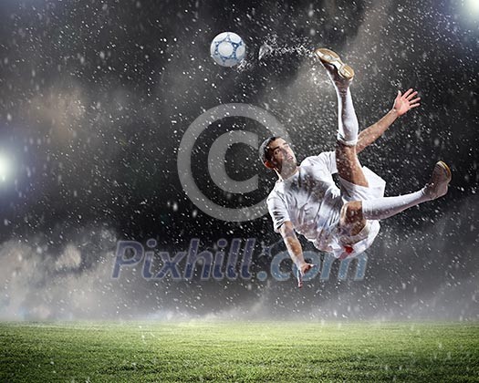 Football player in white shirt striking the ball at the stadium under rain