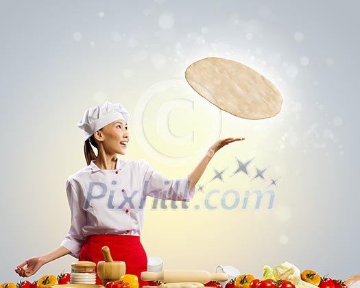 Asian female cook making pizza standing against color background