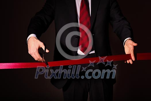 Hand of a businessman with scissors cuting a red ribbon