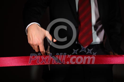 Hand of a businessman with scissors cuting a red ribbon