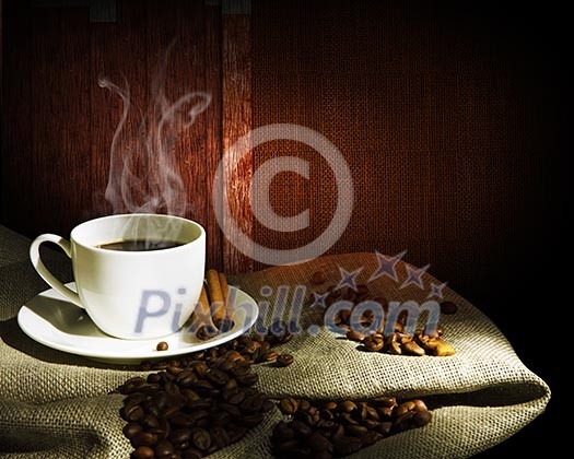 Steaming cup of coffee, cinnamon sticks and a few coffee beans. still life