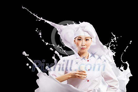 Asian female cook against milk splashes in red apron against black background holding glass of milk
