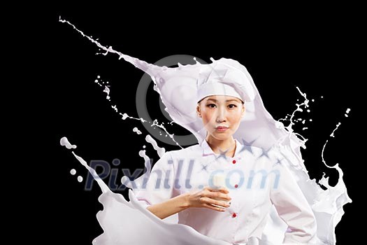 Asian female cook against milk splashes in red apron against black background holding glass of milk Asian female cook against milk splashes in red apron against black background holding glass of milk