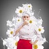 Asian female cook against milk splashes in red apron against flower background drinking milk